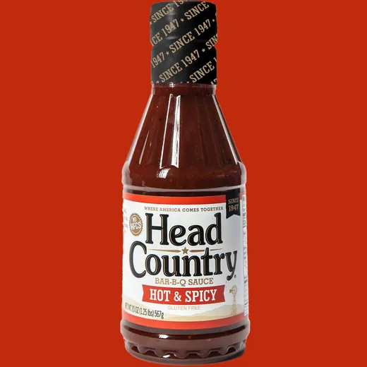 A single bottle of Head Country Hot & Spicy BBQ sauce against a red background.