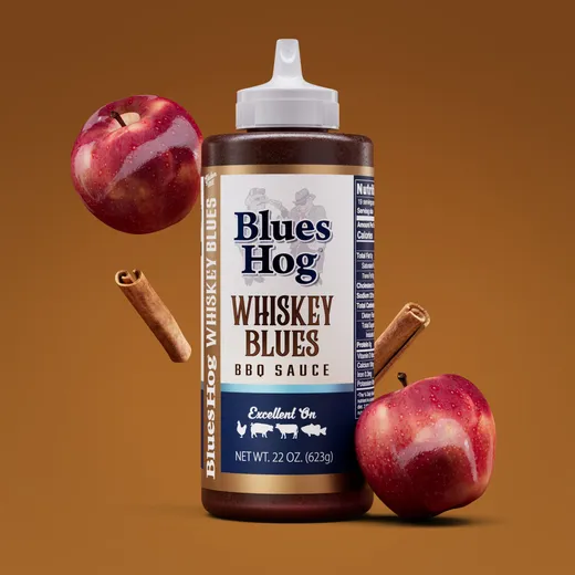Blues Hog Whiskey Blues BBQ sauce bottle surrounded by apples and cinnamon sticks.
