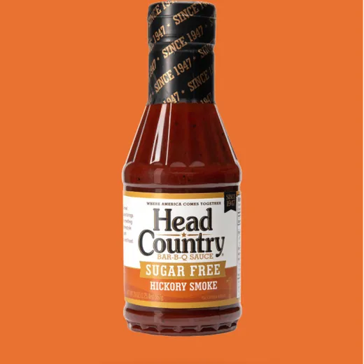 A close-up shot of a bottle of Head Country sugar-free hickory smoke BBQ sauce against an orange background.