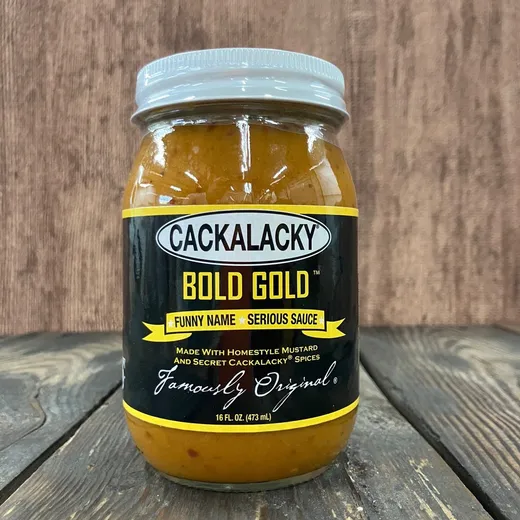 A jar of Cackalacky Bold Gold BBQ sauce on a wooden surface.