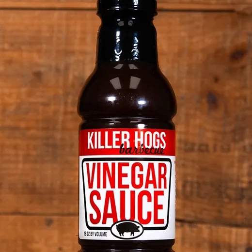 A bottle of Killer Hogs Vinegar Sauce set against a wood background.