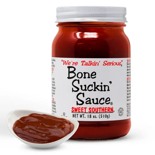 A jar of Bone Suckin' Sauce next to a spoon filled with the sauce.