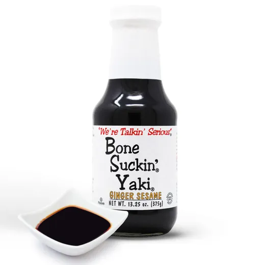 A bottle of Bone Suckin' Yaki Ginger Sesame sauce next to a small bowl of sauce.