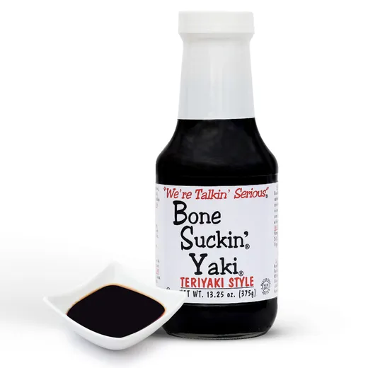 A single bottle of Bone Suckin' Yaki teriyaki sauce next to a small dish of sauce.